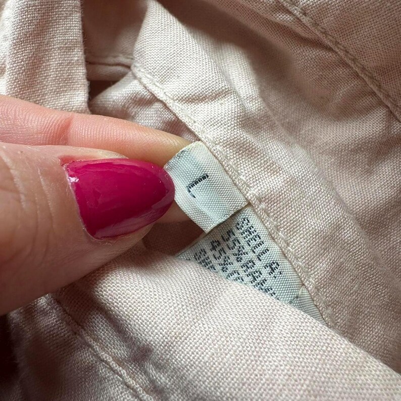 May include: A close-up of a beige fabric shirt with a white tag that says "1" and has additional text in a smaller font.