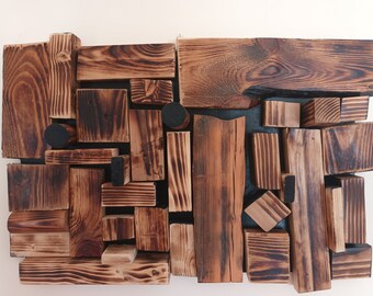 Puede incluir: Una pieza de arte de pared hecha de bloques de madera de varios tamaños, cada uno con un patrón de veta de madera diferente y un acabado carbonizado marrón oscuro, casi negro. Los bloques están dispuestos en un patrón aleatorio, creando un diseño único y moderno.