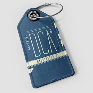 Op de afbeelding: Een blauw bagagelabel met de letters "DCA" in een vetgedrukte, schreefloze letter. Het label bevat ook de tekst "WASHINGTON DC" en het nummer "45-09039". Een zilverkleurige draadlus is aan de bovenkant van het label bevestigd.