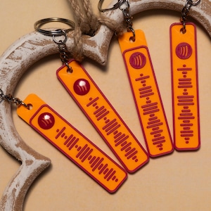 Könnte beinhalten: Vier orangefarbene Schlüsselanhänger mit rotem Spotify-Code-Design. Jeder Schlüsselanhänger hat einen silbernen Ring und eine Kette. Die Schlüsselanhänger sind rechteckig mit abgerundeten Ecken und einem kleinen Loch oben für die Kette.