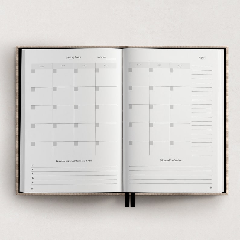 May include: A monthly review planner with a calendar grid, space for notes, and sections for listing important tasks and reflections. The planner has a beige cover and black binding.