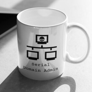 May include: White ceramic mug with a black graphic of a computer network and a skull icon on the top monitor. The text "Serial Domain Admin" is below the graphic. The mug is on a light-colored surface next to a laptop.