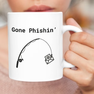 May include: White ceramic mug with the text "Gone Phishin'" and a fishing rod graphic with an email icon as bait. The mug has a white handle and is held by a person.