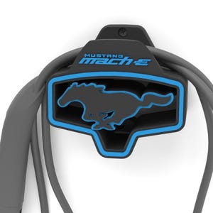May include: Black and blue wall-mounted charging cable holder for a Mustang Mach-E electric vehicle. The holder features the Mustang logo and the text "MUSTANG MACH-E" in blue. The charging cable is gray.
