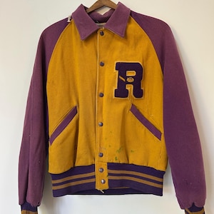 Puede incluir: Una chaqueta universitaria de color amarillo mostaza y morado con un gran parche de la letra R morada en el pecho. La chaqueta tiene cuello, cierre de botones a presión, dos bolsillos laterales y puños y dobladillo acanalados con rayas.