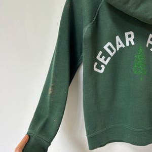 K&ouml;nnte beinhalten: Ein Set aus drei Keramikbechern mit gesprenkelter, cremefarbener Glasur. Jeder Becher zeigt ein handgemaltes Design: ein blau-gr&uuml;nes Blatt, eine gelbe Blume und eine rote Beere. Die Becher haben eine einfache, abgerundete Form und einen bequemen Griff.