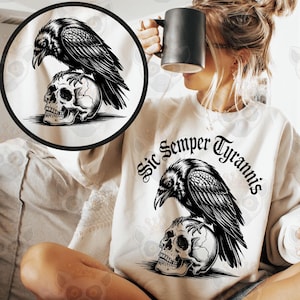 May include: A white sweatshirt featuring a black raven perched atop a skull, with the text "Sic Semper Tyrannis" in a gothic font. The design is centered on the front. The image also includes a black mug.