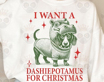 May include: White sweatshirt with a green and red illustration of a dachshund wearing a hippopotamus costume. The text "I WANT A DASHIEPOTAMUS FOR CHRISTMAS" is printed on the sweatshirt.