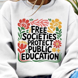 以下が含まれることがあります： 花柄のデザインと「Free Societies Protect Public Education」というテキストが書かれた白いスウェットシャツ。