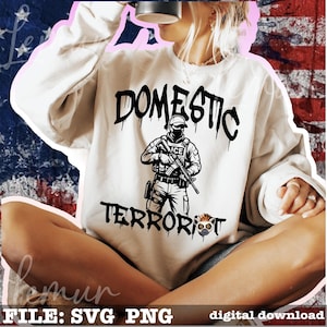 May include: White sweatshirt with a black graphic that reads "DOMESTIC TERRORIST" with an illustration of a person in tactical gear holding a rifle. The text "ICE" is visible on the person's uniform. The words "FILE: SVG PNG" and "digital download" are at the bottom.