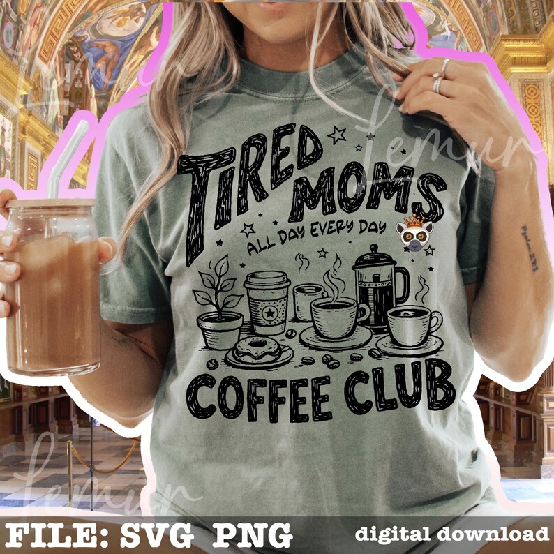 May include: A pale green t-shirt featuring the text "TIRED MOMS COFFEE CLUB" in black, with coffee-themed illustrations. The shirt also displays the phrase "ALL DAY EVERY DAY". A glass of iced coffee is visible.
