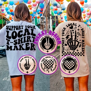 May include: Two white t-shirts with black text and graphics. The front of the shirt says "Support Your Local T-Shirt Maker". The back of the shirt has a graphic of a skeleton hand with a peace sign and the text "Support Your Local T-Shirt Maker".