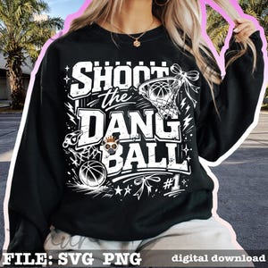 Puede incluir: Sudadera negra con un gr&aacute;fico blanco que dice "Shoot the Dang Ball" con una pelota de baloncesto, una red y estrellas. El dise&ntilde;o incluye un panda de dibujos animados con una corona. Tambi&eacute;n incluye el n&uacute;mero 1.