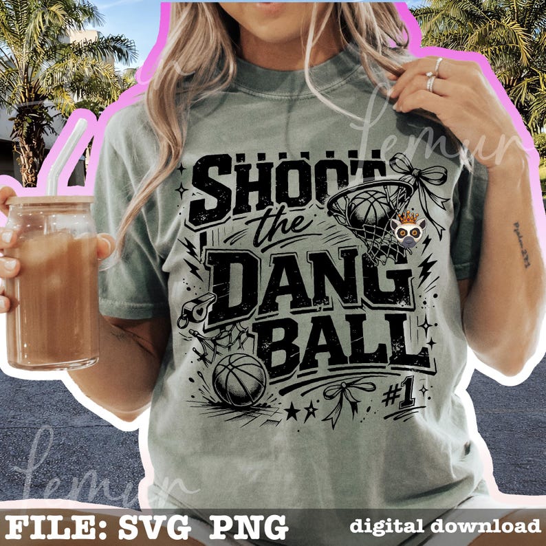 Puede incluir: Camiseta verde claro con el texto negro "SHOOT the DANG BALL". El dise&ntilde;o incluye una pelota de baloncesto, una red y un silbato. La camiseta tambi&eacute;n tiene el n&uacute;mero 1 y estrellas. Un vaso con pajita y bebida se sostiene en la mano izquierda.