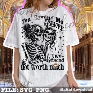 Op de afbeelding: Wit T-shirt met een zwart-witte afbeelding van twee skeletfiguren met zonnebrillen. De tekst luidt "You Remind Me of a Penny, two-faced & not worth much."
