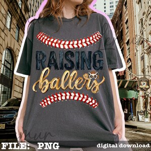 May include: Dark gray t-shirt with the text "RAISING ballers" in a baseball-themed design. The design includes red and white baseball stitching and a cartoon animal wearing a crown. Digital download.