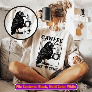 May include: A white sweatshirt with a black graphic of a crow holding a coffee cup, with the text "CAWFEE first THEN THE CHAOS". A black coffee mug is held up near the face. The image also includes a circular graphic of the crow.