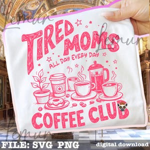 May include: White tote bag featuring a pink graphic with the text "Tired Moms Coffee Club" and coffee-themed illustrations. The design includes a coffee pot, cups, a donut, and a plant. The text "All Day Every Day" is also included.