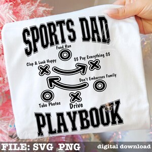 以下が含まれることがあります： 「SPORTS DAD PLAYBOOK」と書かれた黒いグラフィックの白いTシャツ。プレイブックには、「Food Run」、「Clap & Look Happy」、「Take Photos」などの指示が含まれています。シャツは手で持たれています。