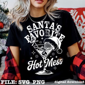 May include: Black t-shirt with a white graphic that reads "Santa's Favorite Hot Mess." The design includes a martini glass with a Santa hat, ice cubes, and stars. The words "FILE: SVG PNG digital download" are at the bottom.