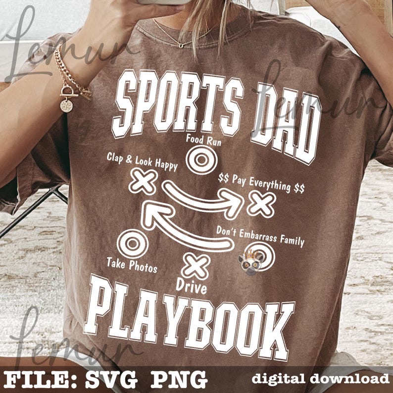 以下が含まれることがあります： 「SPORTS DAD PLAYBOOK」の白い文字が入った茶色のTシャツ。 「Clap & Look Happy」や「Take Photos」などの指示があるフットボールのプレーのグラフィックが特徴です。