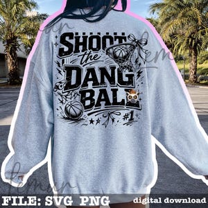 Puede incluir: Sudadera gris claro con un dise&ntilde;o de baloncesto. El dise&ntilde;o presenta el texto "SHOOT the DANG BALL" en negro, junto con balones de baloncesto, una red y un b&uacute;ho de dibujos animados con una corona. Tambi&eacute;n se incluye el n&uacute;mero "#1".