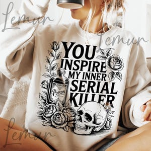 May include: Cream-colored sweatshirt with a black graphic design. The design includes a skull, roses, a poison bottle, and the text "YOU INSPIRE MY INNER SERIAL KILLER."