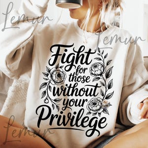 May include: Cream-colored sweatshirt with the text "Fight for those without your Privilege" in black script. The text is surrounded by floral and leaf designs. The sweatshirt is a casual style.