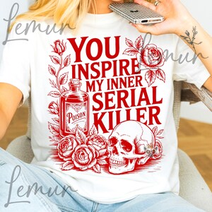 May include: White t-shirt with a red graphic design. The design includes the text "YOU INSPIRE MY INNER SERIAL KILLER", a poison bottle, roses, and a skull. The shirt is a casual wear item.