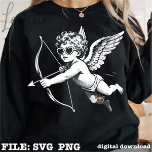 Op de afbeelding: Zwart sweatshirt met een witte illustratie van Cupido met een hartvormige zonnebril, vleugels en pijl en boog. De tekst "FILE: SVG PNG" en "digital download" staat onderaan.