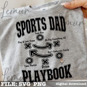 以下が含まれることがあります： 「SPORTS DAD PLAYBOOK」の文字が黒でプリントされたライトグレーのスウェットシャツ。デザインには、フットボールのプレー図と「Clap & Look Happy」や「Take Photos」などのフレーズが含まれています。下部には「FILE: SVG PNG digital download」と記載されています。