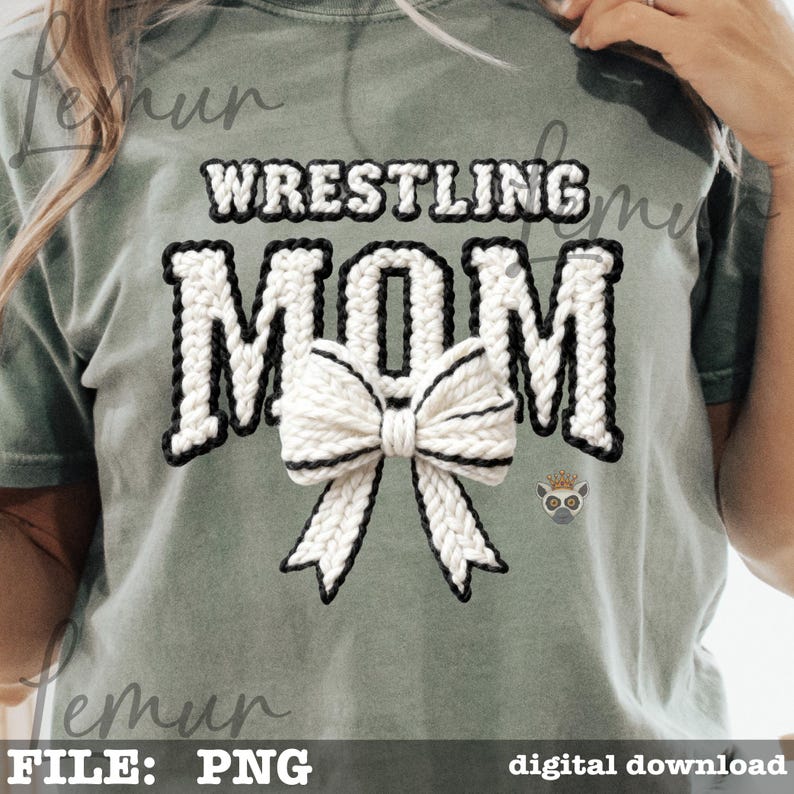 May include: A sage green t-shirt with the words "WRESTLING MOM" in a white, textured font with black trim. A white bow with black trim is centered below the word "MOM". A small lemur graphic is on the lower right.