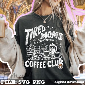 May include: Dark grey sweatshirt featuring the words "Tired Moms Coffee Club" in white. The design includes coffee cups, a coffee pot, a plant, and a donut. The words "All Day Every Day" are also included in the design.