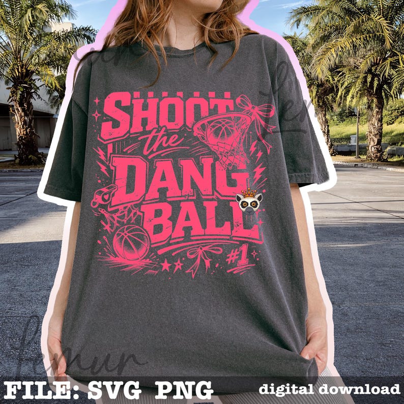Puede incluir: Camiseta gris oscuro con un dise&ntilde;o rosa con tem&aacute;tica de baloncesto. El dise&ntilde;o incluye el texto "Shoot the Dang Ball", una canasta de baloncesto, una pelota de baloncesto y el n&uacute;mero "#1".