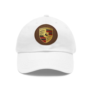 May include: White baseball cap featuring a brown leather patch with the Porsche emblem. The emblem is a shield with the word "Porsche" above a black horse, red and black stripes, and gold accents.