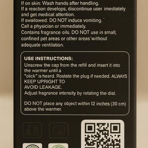 May include: Black box with white text detailing first aid, use instructions, and safety warnings for fragrance oils. Includes a QR code labeled "SCAN ME" and two product certification logos. The text advises against placing objects within 12 inches (30 cm) of the warmer.