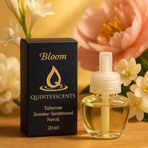 Puede incluir: Un ambientador de cristal transparente con tapa blanca y caja negra. La caja dice "Bloom" y "Quintesscents" con notas de fragancia. El ambientador está junto a flores blancas y rosas. Contiene 20 ml.