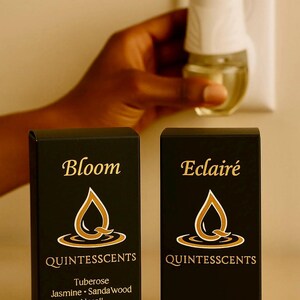 May include: Two black boxes with gold lettering and a matching air freshener. The boxes read "Bloom" and "Eclair&eacute;" with the brand "Quintesscents". The "Bloom" box lists Tuberose, Jasmine, Sandalwood, and Neroli. Each box contains 20ml.