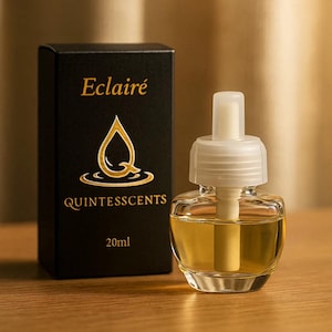 May include: An air freshener with a clear glass bottle and a white top, next to a black box. The box has gold text reading "Eclairé QUINTESSCENTS 20ml" and a gold logo. The bottle contains a yellow liquid.