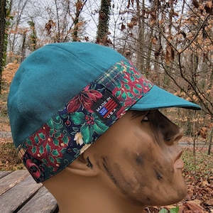 May include: Teal baseball cap with a patterned band featuring red and green floral designs. The cap has a small brim and a label that reads "MADE IN USA".