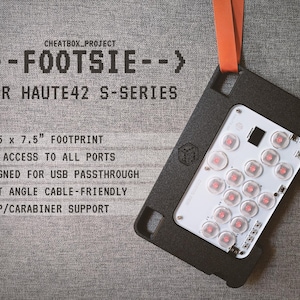 Op de afbeelding: Zwart elektronisch apparaat "FOOTSIE" voor HAUTE42 S-SERIES. Eenvoudige poorttoegang, USB-passthrough en riemondersteuning. Het apparaat heeft een voetafdruk van 28,58 x 19,05 cm en een witte printplaat met rode lampjes.