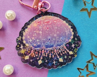 May include: A pink, blue and purple iridescent charm with a galaxy design and a cluster of stars. The charm is attached to a pink metal key chain.