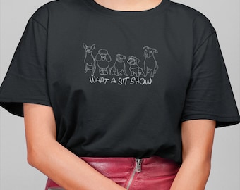 May include: A black t-shirt with a white outline of five dogs sitting in a row. The text "WHAT A SIT SHOW" is printed below the dogs.