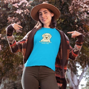 Puede incluir: Una mujer con una camiseta azul con un perro de dibujos animados con gafas y el texto "El cambio de comportamiento lleva tiempo". También lleva una chaqueta de punto marrón y un sombrero marrón.