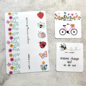 May include: White stickers with spring-themed designs. One sticker has a floral border and the text "spring time vibes." Other stickers feature a strawberry, bee, snail, ladybug, butterfly, flowers, a pink bicycle, and the text "seasons change and so do we."