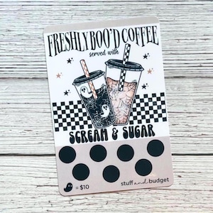 May include: A rectangular card with the text "FRESHLY BOO'D COFFEE" and "SCREAM & SUGAR" in a spooky font. The card features two coffee drinks with ghost and spiderweb designs, and a series of black circles.