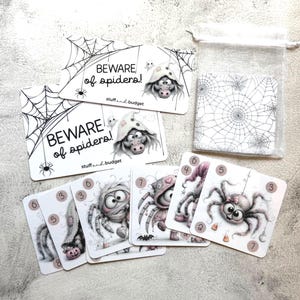May include: A set of rectangular cards featuring black and white spider web illustrations and cartoon spider characters. The cards display the text BEWARE of spiders! and stuff and budget. Includes a sheer white drawstring pouch for storage.