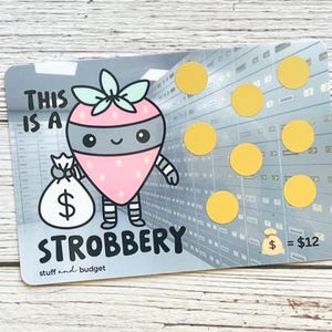 May include: A novelty scratch-off card featuring a cartoon strawberry character in a bandit mask holding a money bag. The card has the text "THIS IS A STROBBERY" and "stuff and budget". There are yellow scratch-off circles and a $12 value.
