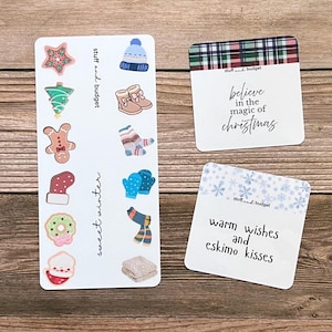 May include: A collection of winter-themed stickers and cards. The stickers feature festive designs like a star, tree, gingerbread man, and mittens. The cards have text that reads "believe in the magic of christmas" and "warm wishes and eskimo kisses."