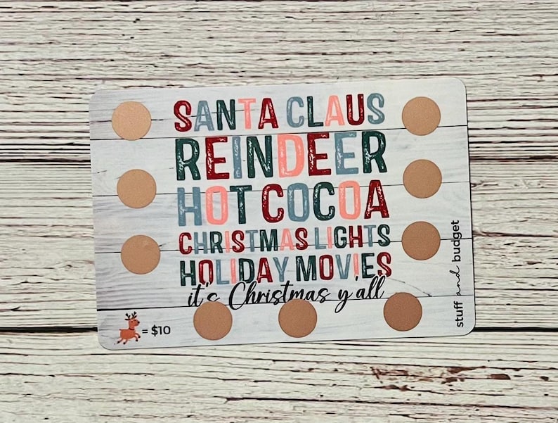 May include: A white card with a woodgrain background and brown circles. The card has the text "Santa Claus, Reindeer, Hot Cocoa, Christmas Lights, Holiday Movies, It's Christmas y'all" in colorful letters. The card also has the text "stuff and budget" and a reindeer with the text "= $10".